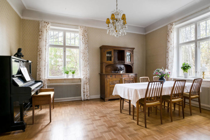 Mysig matsal i äldre villa från 1912 med piano, kristallkrona och traditionella möbler.