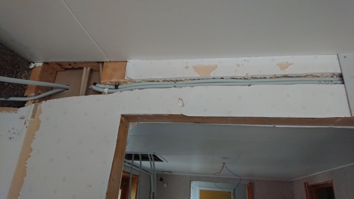 Elektriska kablar dragna genom urgröpt område i bärande vägg med synliga skador och avskalad väggbeklädnad.