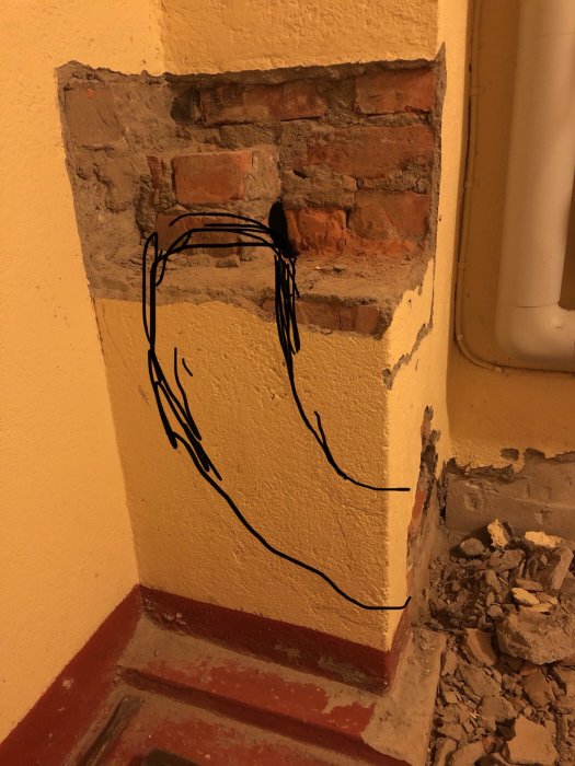 Delvis nedbruten murad vägg med synlig tegelstruktur och en svart skiss som visar planerat hål.