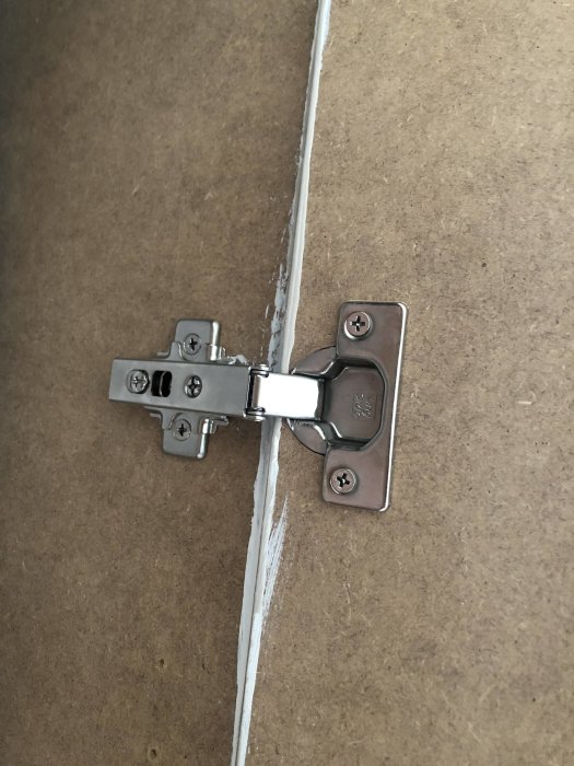 Gångjärn monterat på en skåpdörr med synliga skruvar och exakta mätningar för placering.