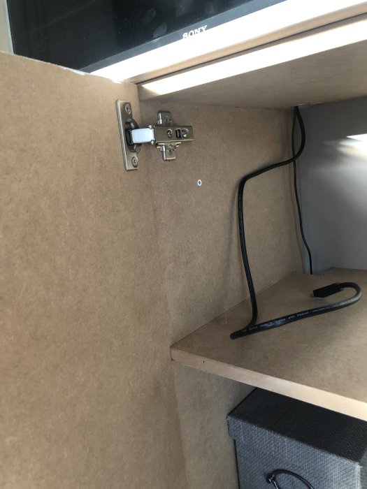 Detaljbild av ett gångjärn som monterats i ett skåp, visar noggrann mätning och installation.