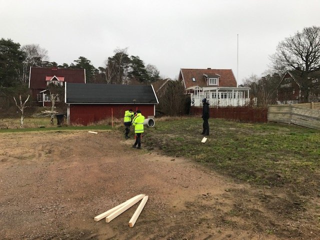 Utstakning av tomt för husbygge i Mellbystrand med arbetare, verktyg och träpaneler på marken.