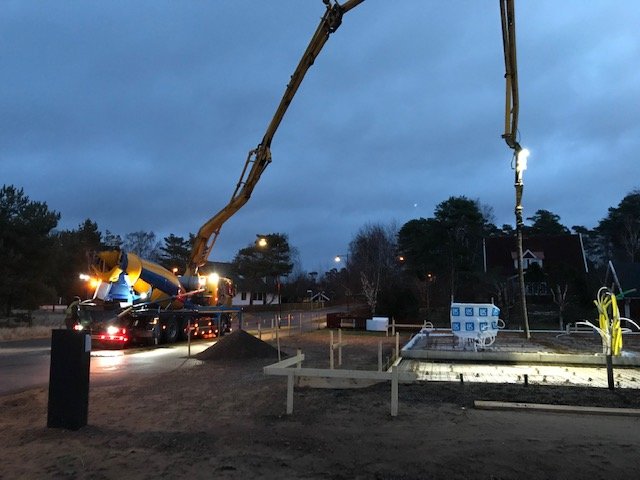 Betongpumpbil häller betong för grundläggning av hus vid gryning.