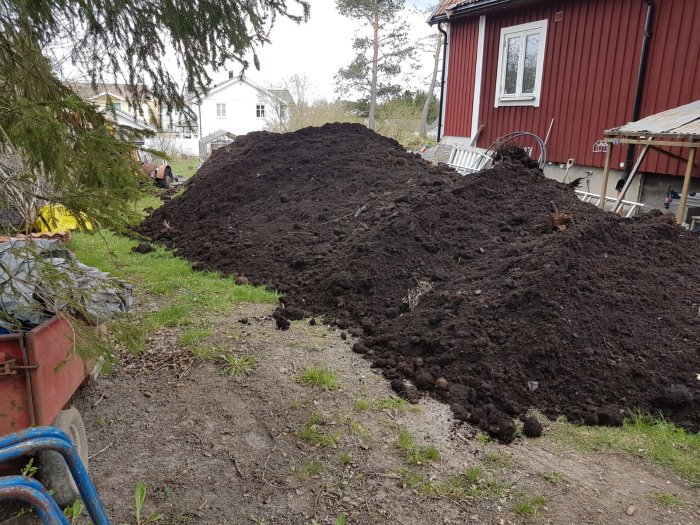 Flera högar av matjord i en trädgård med röd stuga i bakgrunden.