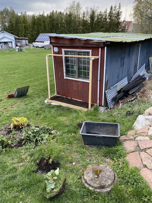 Redskapsbod i trädgård med nybyggd odlingslåda, avtäckt berg, och solpaneler i bakgrunden.