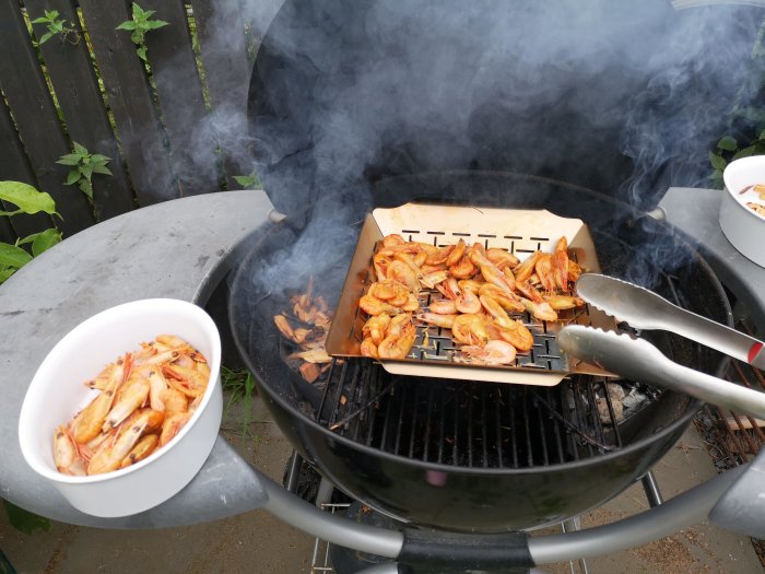 Rökta räkor på grillen med rökspån, serverade med aioli, mycket rök syns runt grillen.