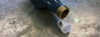 En blå rörsektion med gängad anslutning och en plastbackventil på ett betonggolv.