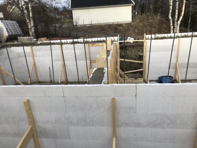 Nybyggd källarvägg i betongblock med stöttande träreglar och synligt spiro-rör för ventilation.