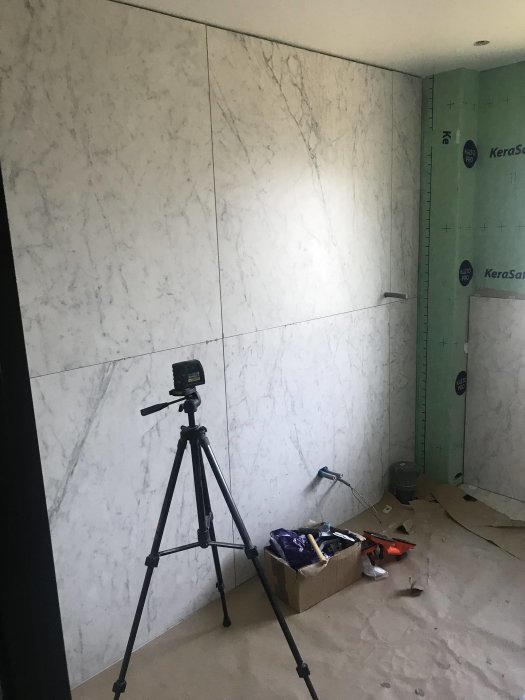 Marble tiled wall in progress with tools and tripod, unfinished section to the right.