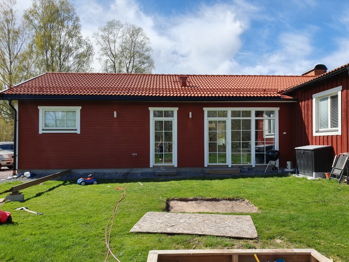 Röd trävilla med sluttande trädgård och markering för däckbygge i nivå med inomhusgolv.