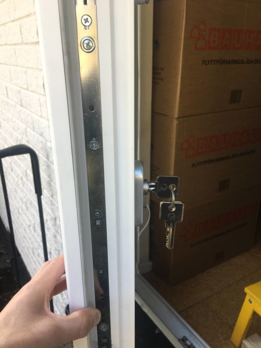 Nyckel i låscylinder på en vit dörr med två synliga skruvar i metallramen vid cylinderns höjd.