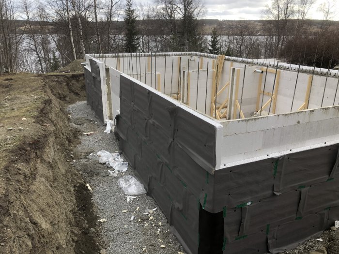 Grund av hus under uppbyggnad med dräneringsskivor och nyligen kopplat avloppssystem vid en sjö.