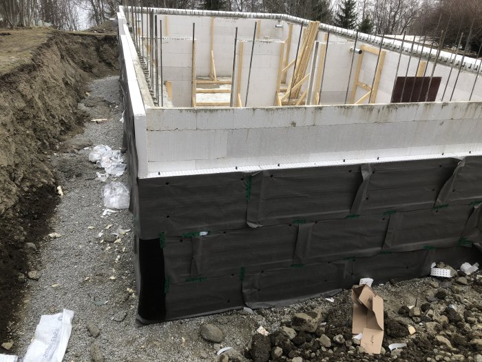 Montering av dräneringsskivor på grunden till ett pågående byggprojekt med synligt avlopp.