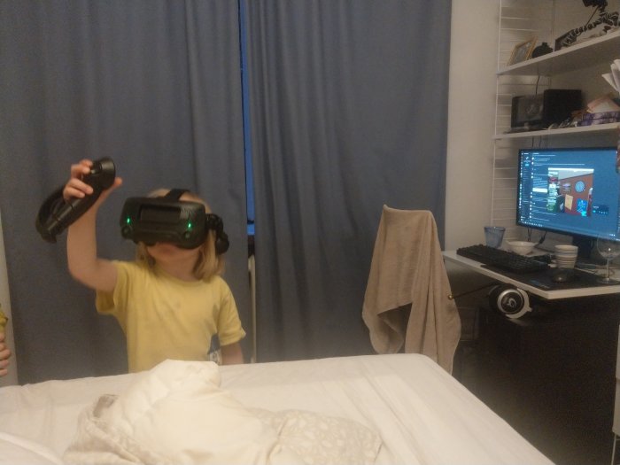 Barn i gult linne använder VR-headset och handkontroller med dator och skrivbord i bakgrunden.