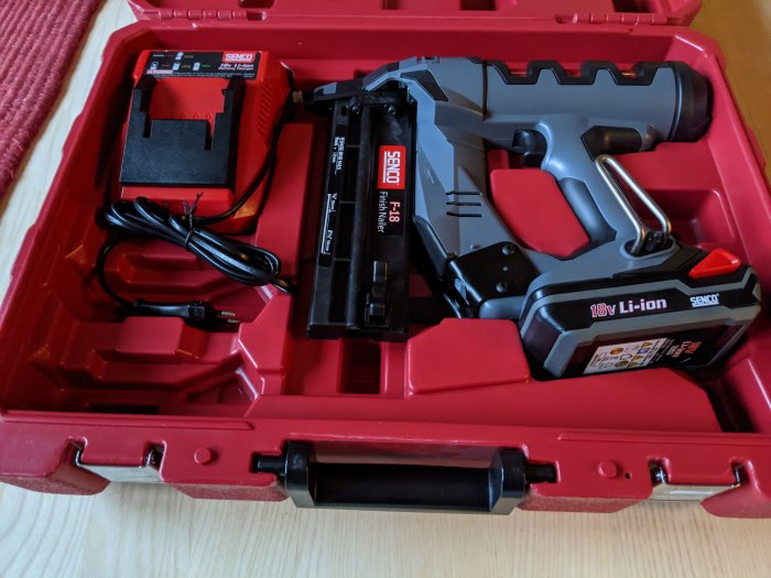 Batteridriven dyckertpistol med batteri och laddare i en öppen röd verktygslåda.