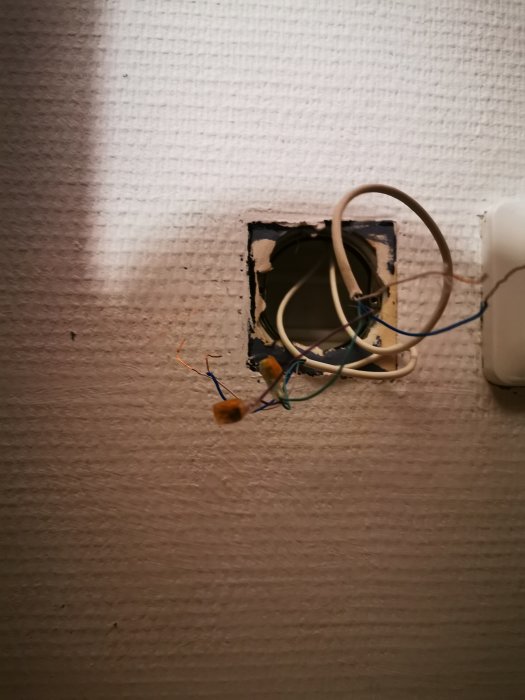 Öppet gammalt telefonuttag med utdragna kablar på en tapetserad vägg.