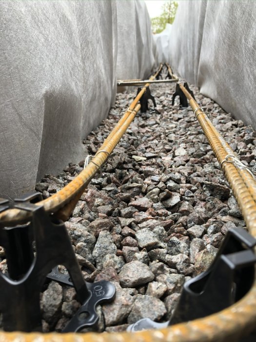 Armeringsjärn bundna längs en ränna av grus med plastskenor och svart klämma.