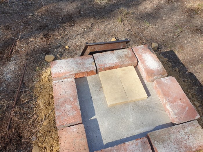 Grundplatta med gjuten betong och tegelstenar för att bygga rökskåp, inklusive en gammal spislucka.