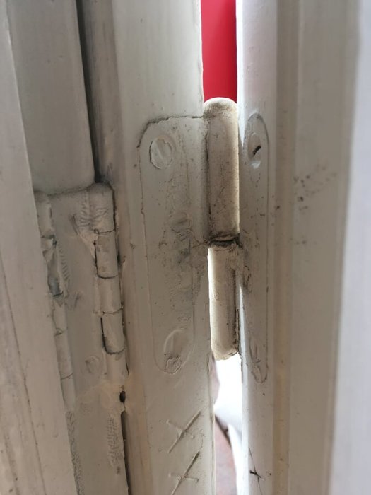 Närbild på övre och nedre gångjärn på en sned hängande balkongdörr, övre gångjärnet har större mellanrum.