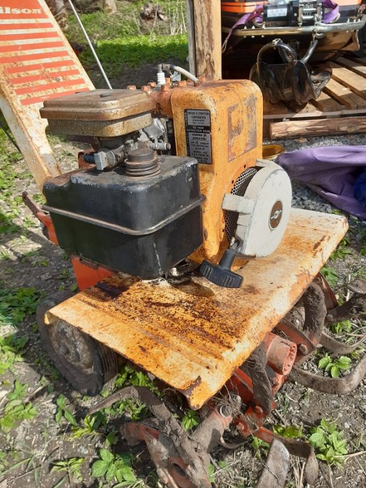 En rostig, orange Gilson jordfräs från 1973 på en träplattform utomhus, med synliga tandskivor och motor.