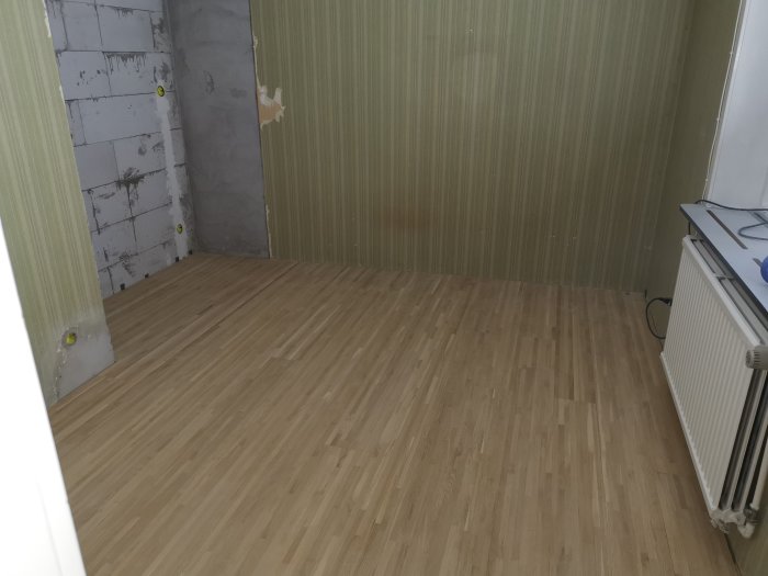 Nyslipat parkettgolv i källarrum med oputsade väggar och tapet.