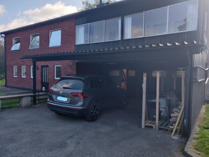 Bilen parkerad under en carport med takstöd och IPE-balk i anslutning till en tegelbyggnad.