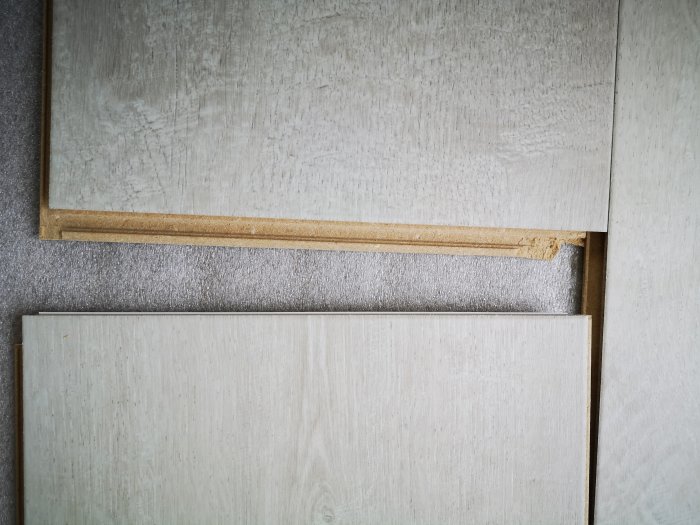 Två ljusa Pergo-laminatplankor med synlig höjdkantförskjutning och en fasad kant, som ligger på ett underlag.