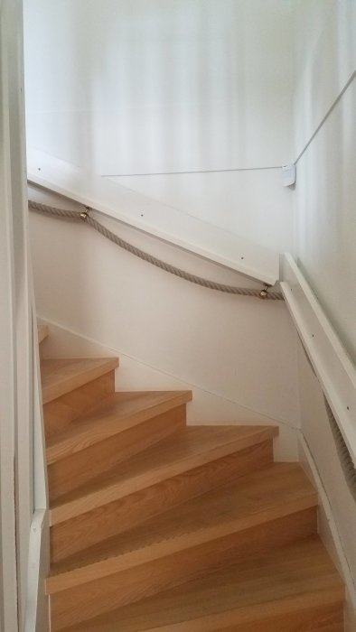 En Ajax-detektor monterad 2 meter högt på en vit vägg ovanför en trätrappa, täcker hela trappområdet.