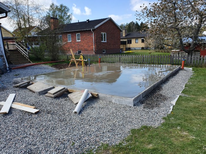 Nyligen gjuten betongplatta med Leca-block på grus, redo för byggstart, omgiven av gräsmatta och staket.