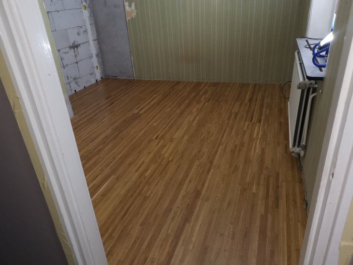Nylackat trägolv i ett renoveringsrum med synliga kabelrör och slipmaterial.