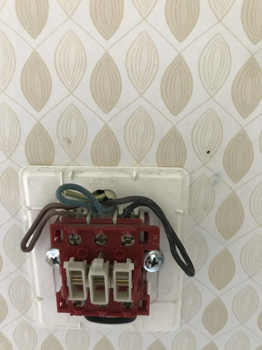 Elektrisk dosa med avklippta kablar och brytare framför kakelvägg.