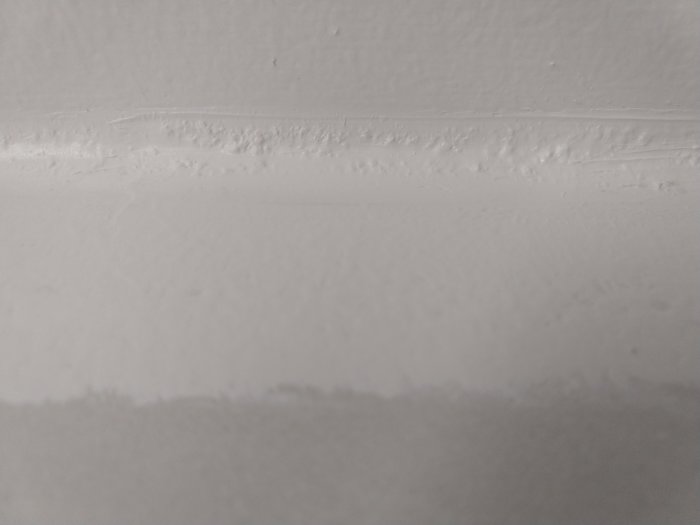 Vägg med nydragen, klumpig och ojämn fogmassa som ser gulaktig och rinnig ut.