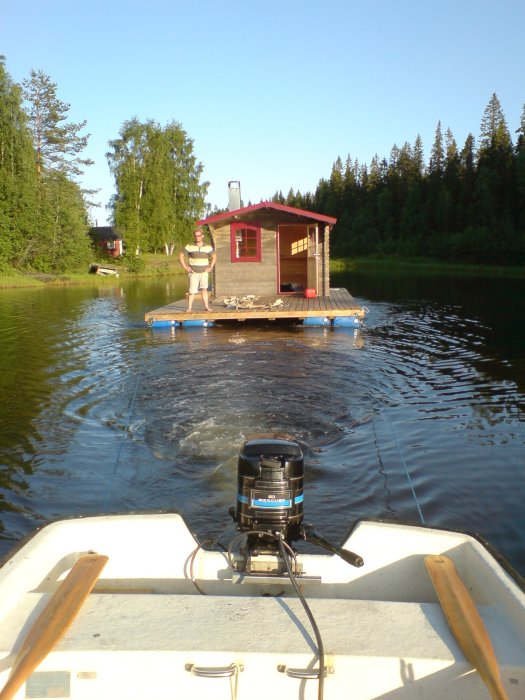 Bastuflotte med person ombord, sedd från en mindre båt på en sjö.