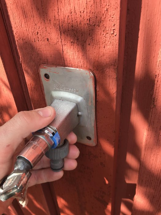 Hand håller en skruvmejsel mot en fastskruvad dörrhandtagplatta på en röd dörr.