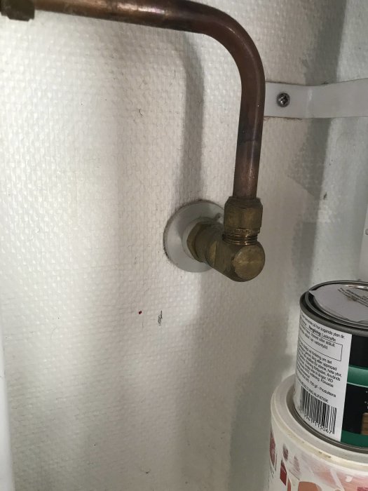 Kopparledning och mässingsventil mot vit texturerad vägg inomhus.