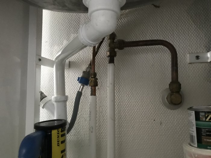 Inre vinkel på rörkonstruktion under diskbänk med synliga avloppsrör och vattenledningar.