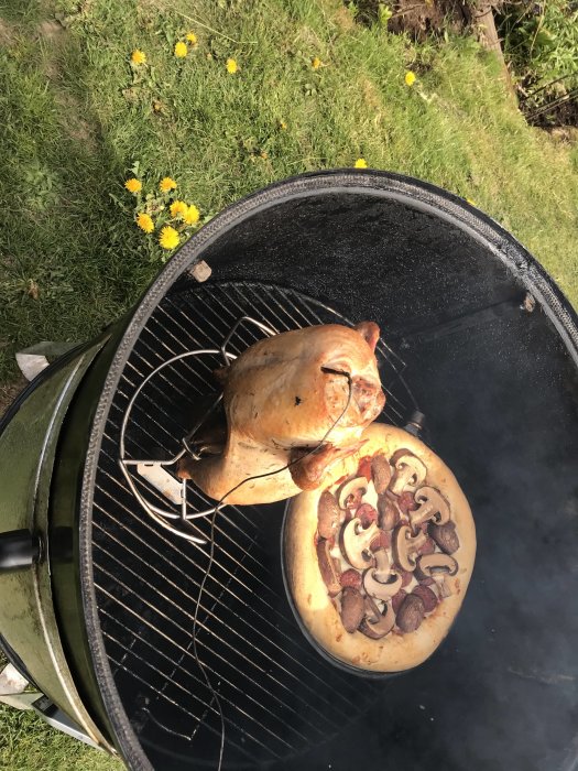 Grillad kyckling över ölburk bredvid en pizza med svamp på en rund grill.