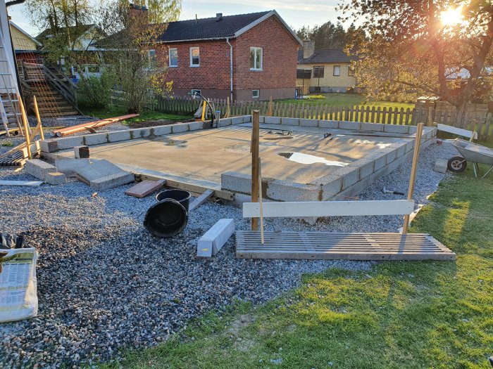 Grundläggning för byggprojekt med betongplatta, grus och material framför hus.