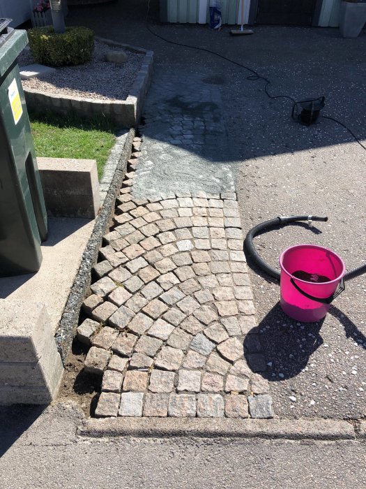 Nyröjd och lagad gatsten i olika nyanser på en uppfart med hink och slang i förgrunden.