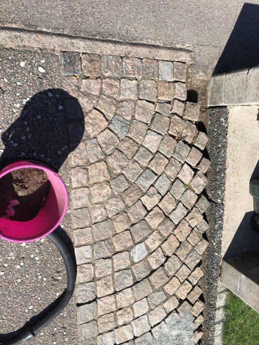 Renoverad gatsten på en framsida med nyinlagda stenar i varierande färger och en tom hink.