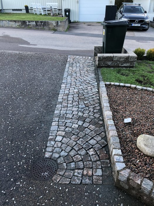 Renoverad gatsten i olika nyanser på en uppfart med grannlåtande gräs och grusytor.