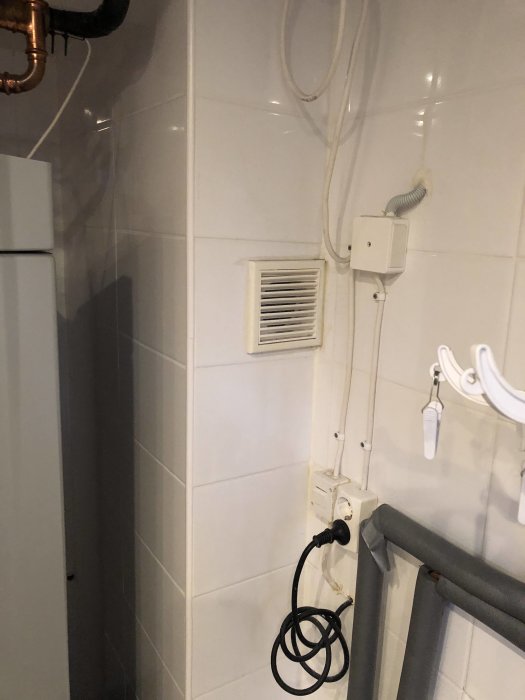 Väggmonterad tilluftsventil i ett kaklat utrymme med synliga rör och elkablar.