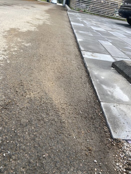 Uppfart med nyupplagda grå stenplattor gränsande mot en äldre asfaltsyta, innan finjustering av övergången.