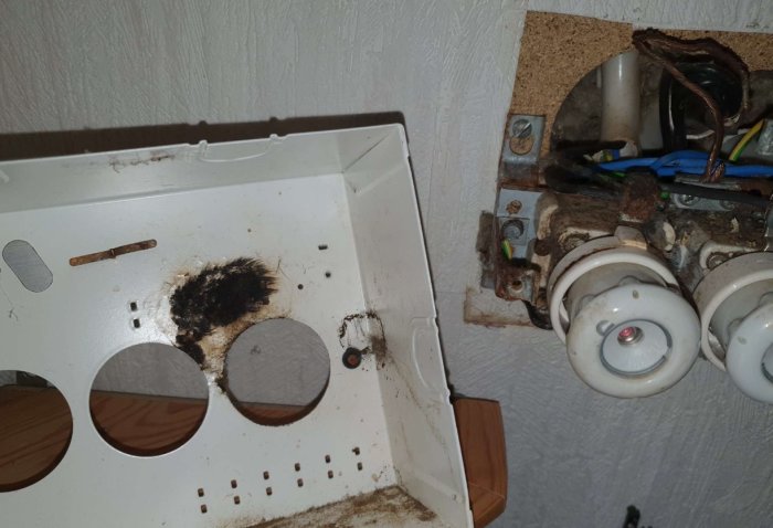 Skadad elcentral med brännskador och en död mus, bredvid gammal elektrisk utrustning i dåligt skick.