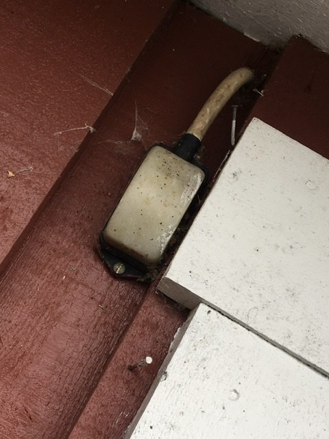 Äldre strömbrytare med kabel monterad på en vägg vid en garagedörr, omgiven av spindelväv.