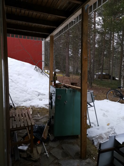 Två trästolpar som stöttar upp en balkong med synlig snö och skog i bakgrunden.