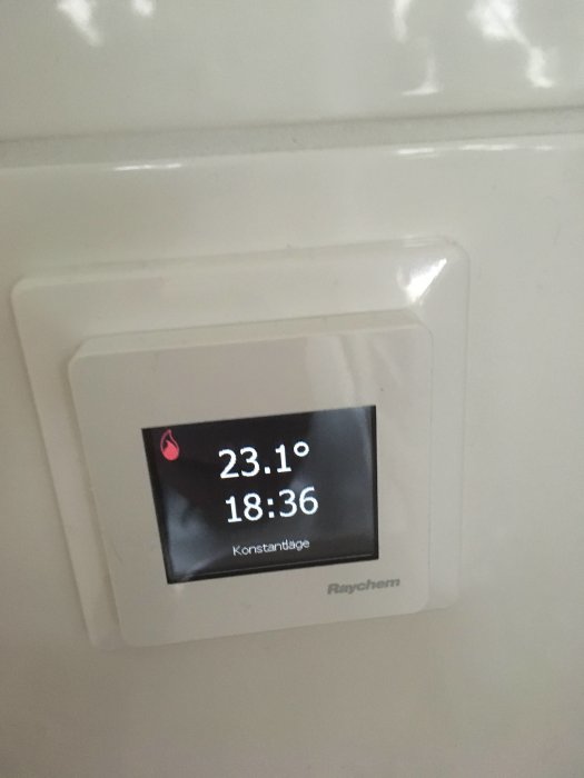 Digital termostat visar 23.1 grader och klockan 18:36 på en vit vägg.