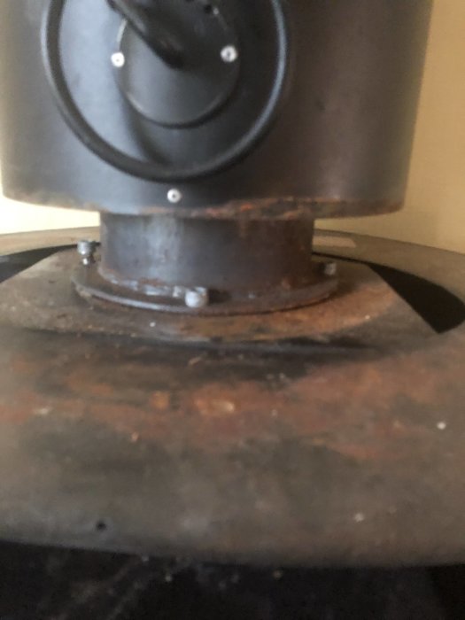 Närbild på en gammal kamin monterad på en rostig metallplatta med bultar, i behov av demontering.