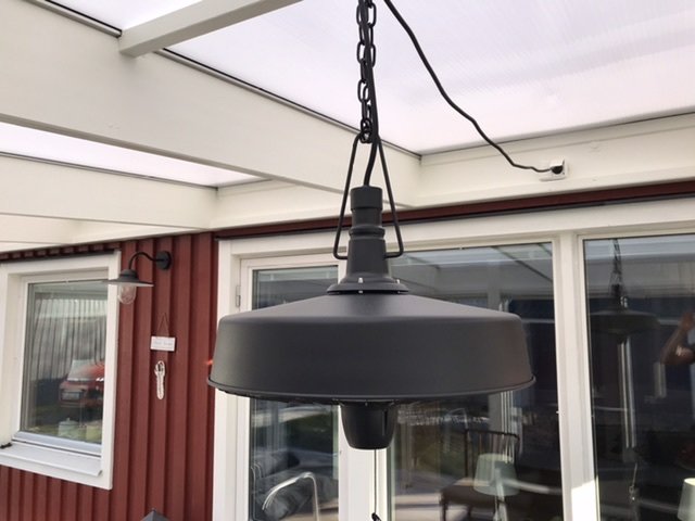 Hängande lampa i uterum med tak och glaspartier i bakgrunden.