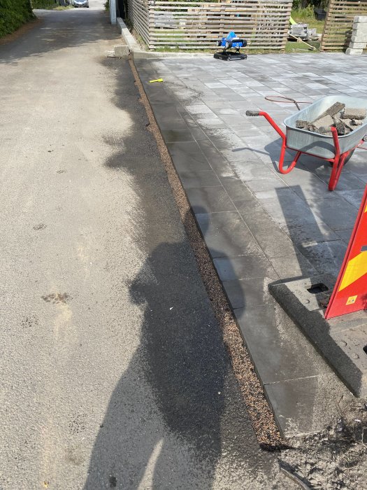 Reparationsarbete på uppfart med nyasfalterad kant, verktyg i bakgrunden, vagnar i förgrunden.